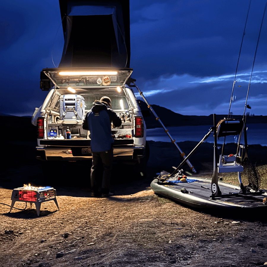 Truck at a lake camp at dusk with the tailgate lit for cooking