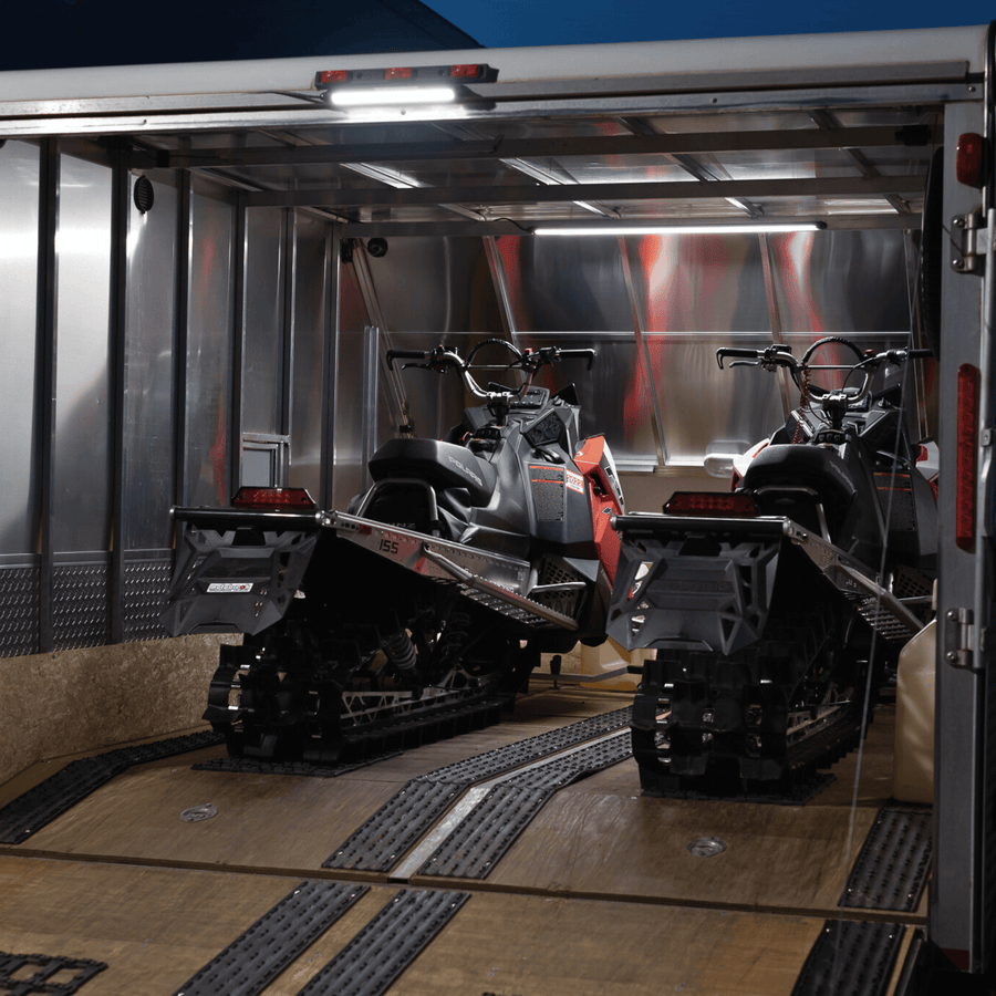 Two snowmobiles in an enclosed trailer lit by two Kingpin lights