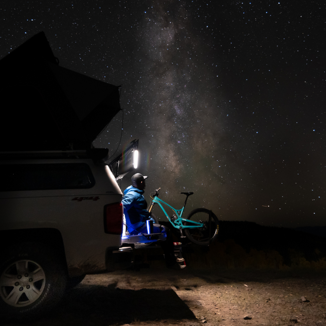 Person with a bike next to a truck at night under the stars, lit by a Kingpin light