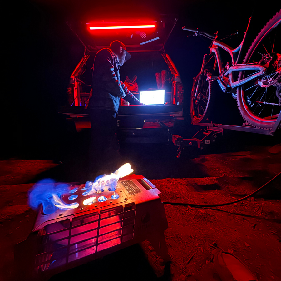 SUV hatch lit red by a Kingpin light at a night camp with a bike and a campfire