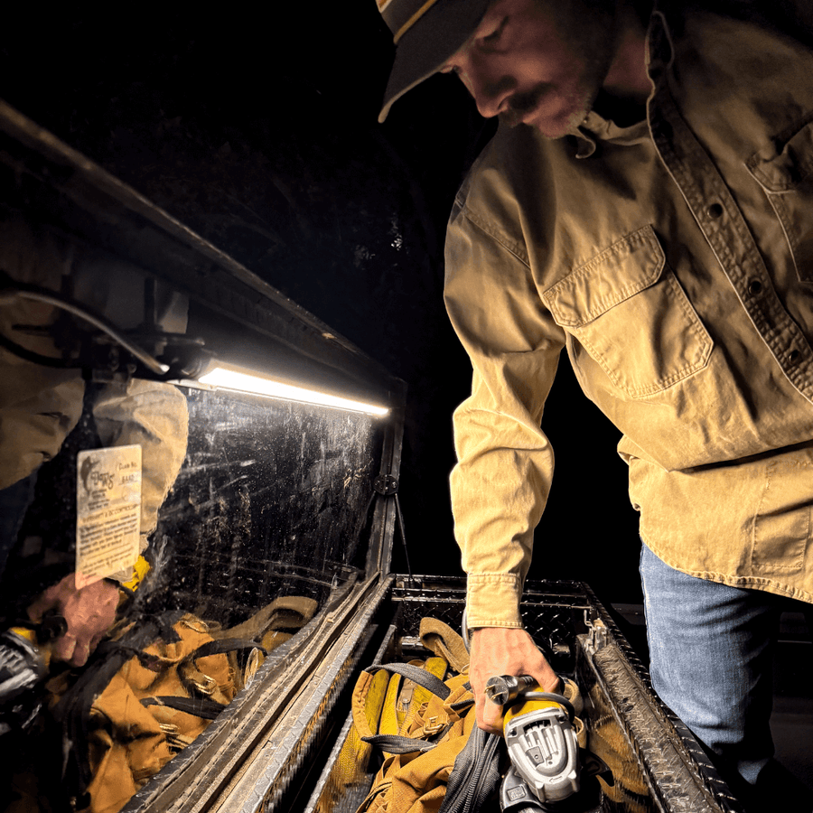 Man reaching for gear in a truck bed toolbox lit by a Kingpin light
