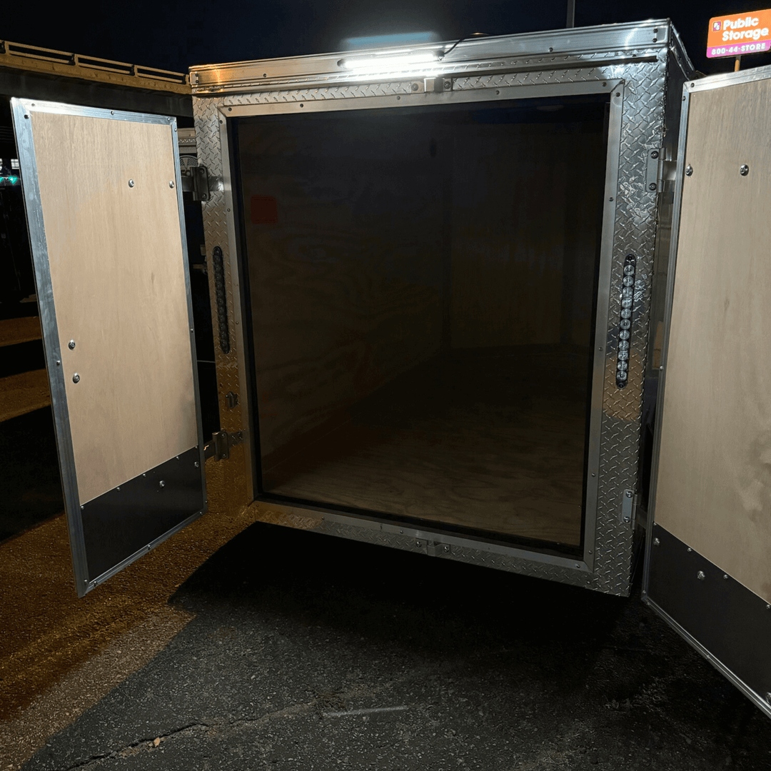 Kingpin v-Series 12" LED light on rear of small, enclosed adventure trailer brightly illuminating ground below and behind. 