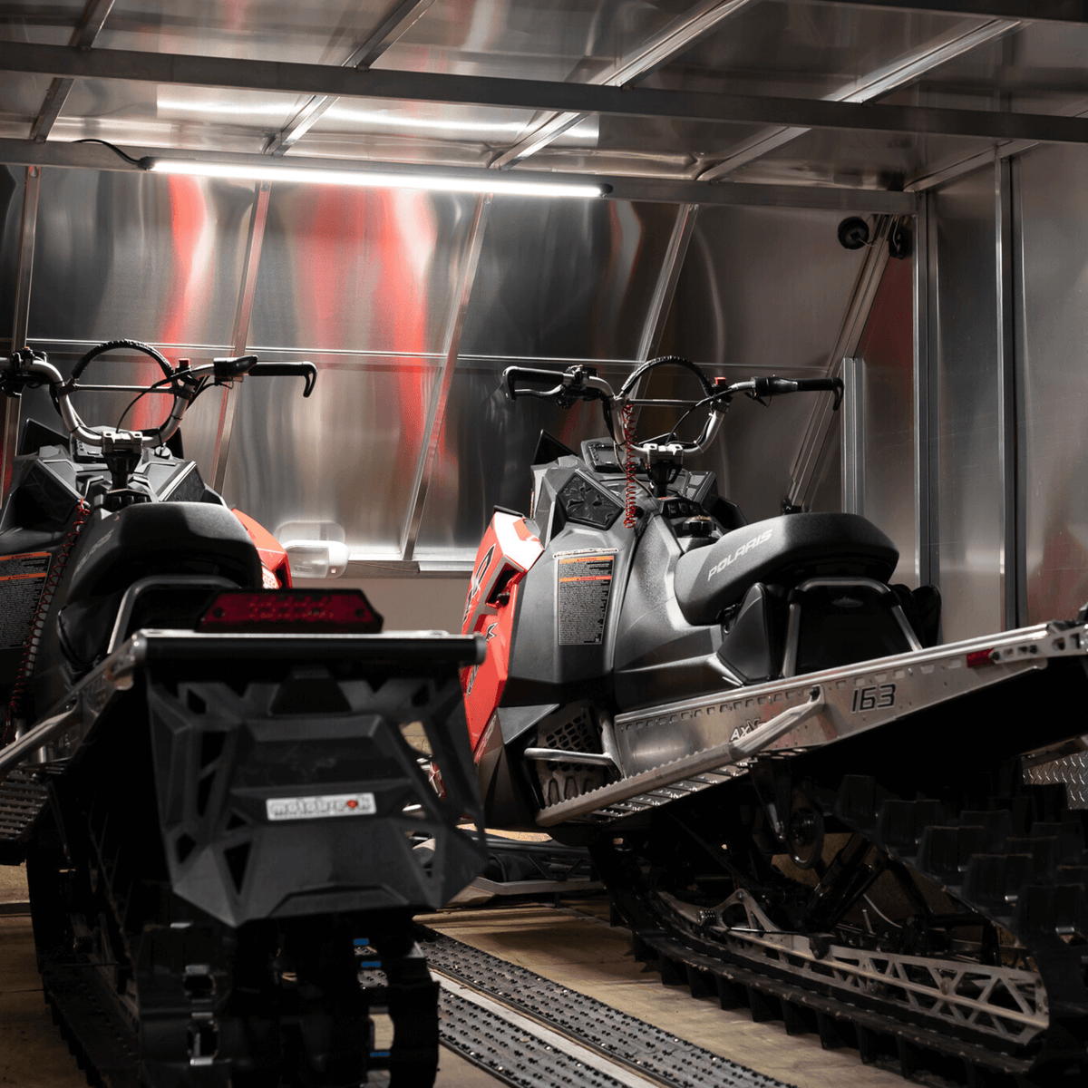 Two snowmobiles in an enclosed trailer lit by a Kingpin light