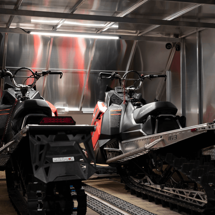 Two snowmobiles in an enclosed trailer lit by a Kingpin light
