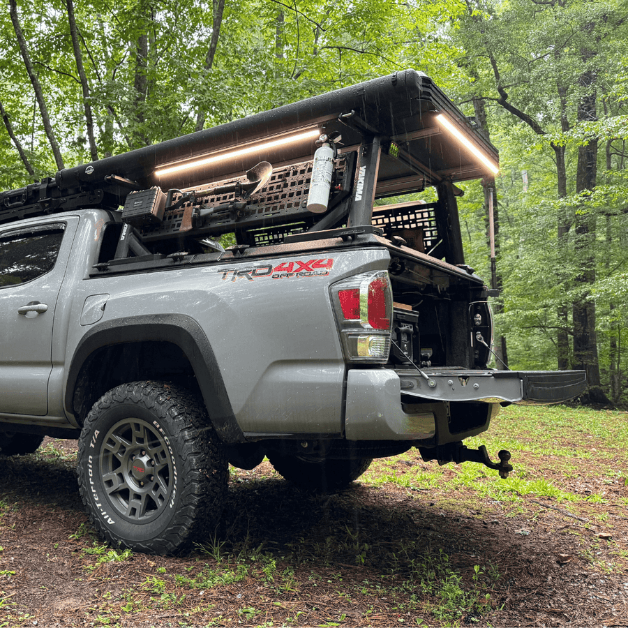 Pickup with a bed rack and Kingpin lights in a forest campsite
