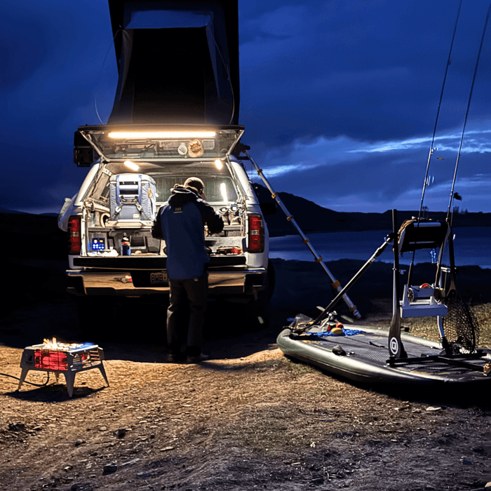 Truck at a lake camp at dusk with the tailgate lit for cooking