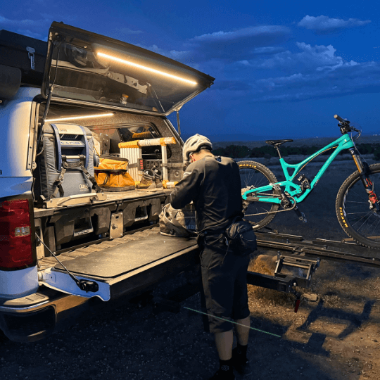 Man loading a mountain bike at a truck cap lit by a Kingpin light