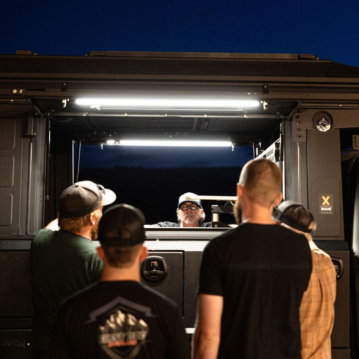 Group of people looking into a truck camper lit by Kingpin lights at dusk