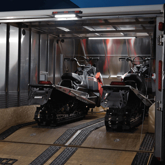 Two snowmobiles in an enclosed trailer lit by two Kingpin lights
